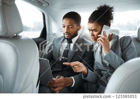 African American man and woman in business attire are working in a car. They are both focused on their work, which suggests they are serious and dedicated to their business. 123365853