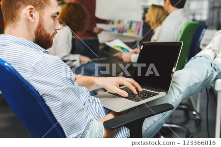 Focused millennial man browsing on laptop with blank screen in modern office, free space 123366016