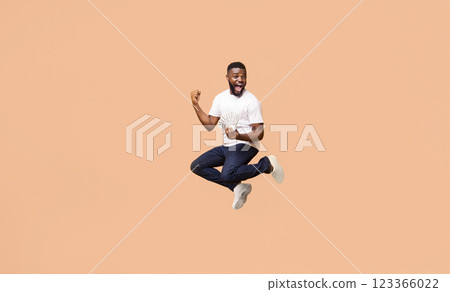 Happy, young black man jumping in air. He is wearing a white t-shirt, blue jeans, and white sneakers. He is holding a wad of cash in his left hand and his right arm is raised in the air, copy space Happy, young black man jumping in air. He is wearing a white t-shirt, blue jeans, and white sneakers. He is holding a wad of cash in his left hand and his right arm is raised in the air, copy space 123366022