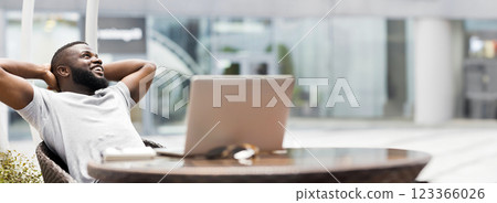Satisfied with work done. Young african american freelancer guy enjoying sunny summer day outdoor in a cafe, panorama 123366026