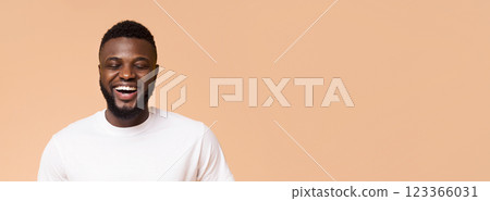 A young African American man with a beard is smiling and looking down. He is wearing a white t-shirt and is standing against a peach background, panorama with copy space A young African American man with a beard is smiling and looking down. He is wearing a white t-shirt and is standing against a peach background, panorama with copy space 123366031