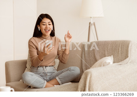 Asian Girl Listening Music in Airpods and Singing Song on Sofa, Free Space 123366269