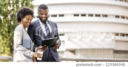 Two smiling african coworkers checking financial reports outdoors, woman having coffee, copy space 123366348