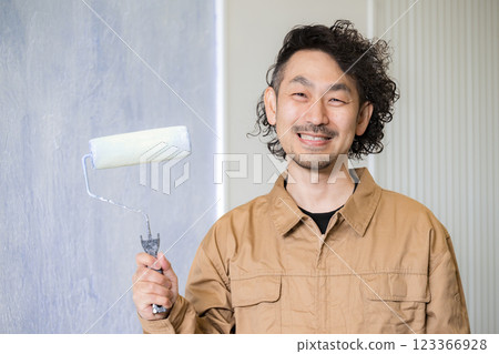 照片中,一名從事繪畫和室內設計行業的男子麵帶微笑,正在粉刷牆壁,同時看著鏡頭 照片中,一名從事繪畫和室內設計行業的男子麵帶微笑,正在粉刷牆壁,同時看著鏡頭 123366928