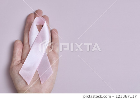 The concept of raising awareness about breast cancer. The hand holds a pink ribbon, a symbol of the fight against the disease. Copy space. The concept of raising awareness about breast cancer. The hand holds a pink ribbon, a symbol of the fight against the disease. Copy space. 123367117