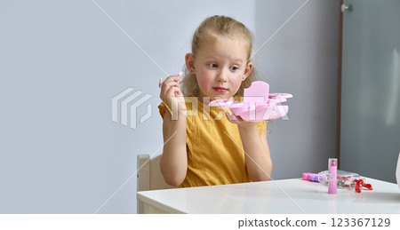 A little girl paints her eyelids with baby shadows. The child paints with children's cosmetics. A daughter imitates her mother 123367129