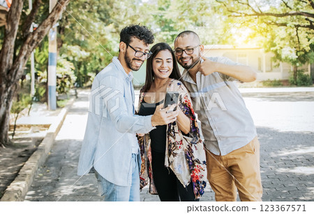 Happy friends watching a cell phone in the street. Three happy friends sharing the cell phone in the street. Concept of happy friends sharing media on a phone Happy friends watching a cell phone in the street. Three happy friends sharing the cell phone in the street. Concept of happy friends sharing media on a phone 123367571