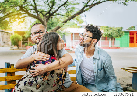 Unfaithful girlfriend hugging her boyfriend in a park secretly kissing another man. Couple infidelity concept, Unfaithful woman sitting hugging her boyfriend and secretly kissing another man. 123367581