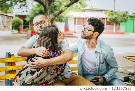 Disloyal girlfriend hugging her boyfriend in a park secretly kissing another man. Couple infidelity concept, Unfaithful woman sitting hugging her boyfriend and secretly kissing another man. 123367582