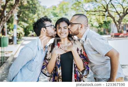 Two men kissing a girl cheek. Portrait of two guys kissing a girl cheek. Two young men kissing a woman cheek outdoor, love triangle concept. Polygamy concept 123367590