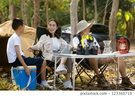 The family of three sitting together in front of the camping tent. The mother is talking to her son. 123368719