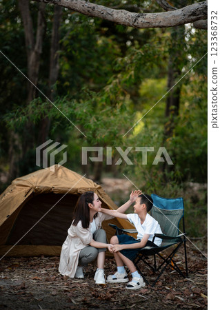 The mother is smiling while giving her son a head pat in front of the camping tent. 123368732