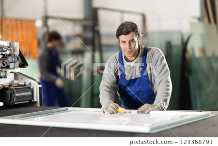 In workshop for production of glass products, man co-worker cuts off excess from workpiece In workshop for production of glass products, man co-worker cuts off excess from workpiece 123368791