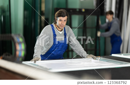 Adult man puts sheet of glass for processing Adult man puts sheet of glass for processing 123368792