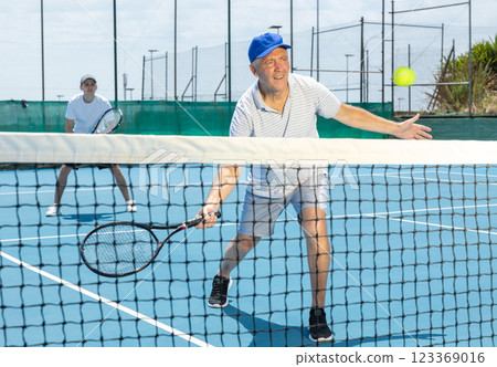 Elderly male player serving ball during training tennis in court outdoors Elderly male player serving ball during training tennis in court outdoors 123369016