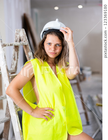 Sexy young woman in a yellow vest and protective helmet poses playfully in renovated room 123369180