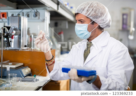Middle-aged Latin male scientist researcher holding tripod and looking at reaction in test tube while performing biochemical tests in lab Middle-aged Latin male scientist researcher holding tripod and looking at reaction in test tube while performing biochemical tests in lab 123369233