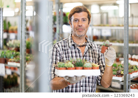 Positive man holding potteds with cactuses in flower shop 123369243
