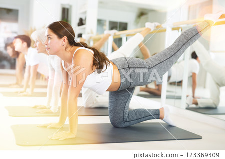 Positive young female performing set of exercises on a pilates mat during group class in fitness studio. 123369309