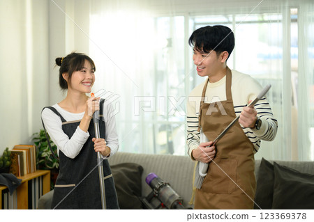 Playful couple wearing aprons cleaning their home. Chores and home care concept Playful couple wearing aprons cleaning their home. Chores and home care concept 123369378