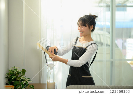 Smiling young asian woman in an apron dusting and cleaning her home 123369393