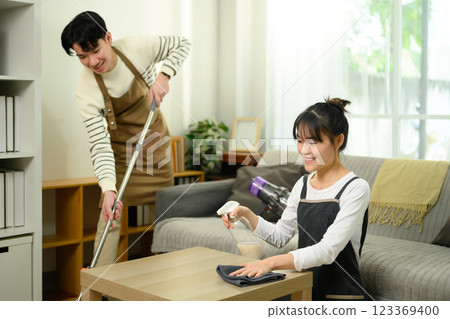 Cheerful young couple works together to clean their living room Cheerful young couple works together to clean their living room 123369400
