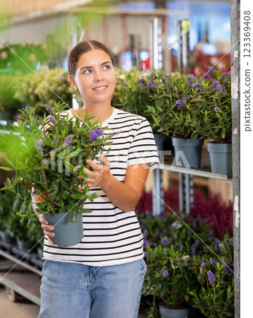Smiling girl choosing potted blooming hebe bush in plant store 123369408