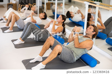 Active vigorous man performs exercises with a pilates roller while on a mat in the hall of a modern fitness studio. Active vigorous man performs exercises with a pilates roller while on a mat in the hall of a modern fitness studio. 123369416