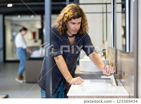 in plumbing department,thoughtful man inspects round white ceramic sinks with faucets 123369434