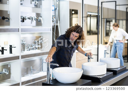 in plumbing department,thoughtful man inspects round white ceramic sinks with faucets in plumbing department,thoughtful man inspects round white ceramic sinks with faucets 123369500