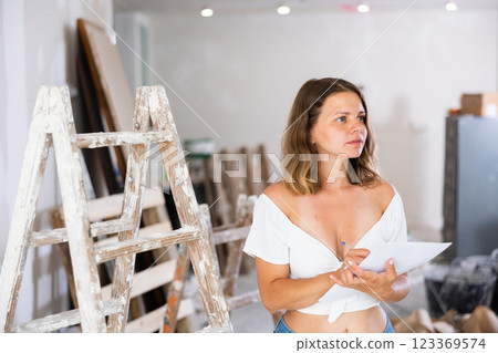 Woman with documents in her hands checks the quality of the completed repairs in cottage room 123369574