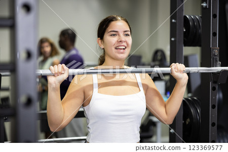 Caucasian woman training with barbell using squat rack in gym Caucasian woman training with barbell using squat rack in gym 123369577