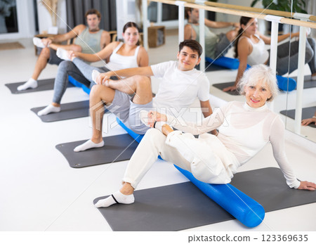 Elderly woman practicing pilates with roller on gray mat in gym room 123369635