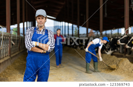 Confident middle-aged man, owner of farm looking at camera with crossed hands on chest in cowshed Confident middle-aged man, owner of farm looking at camera with crossed hands on chest in cowshed 123369743