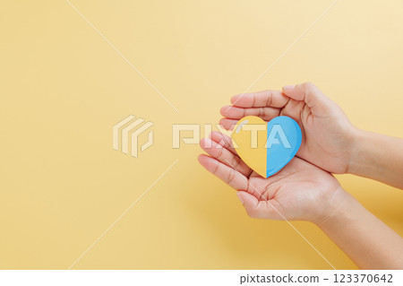 Yellow background with hands holding a divided yellow-blue heart marks Down Syndrome Day. 123370642