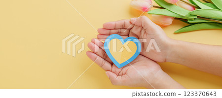 Yellow background with hands holding a divided yellow-blue heart marks Down Syndrome Day. 123370643