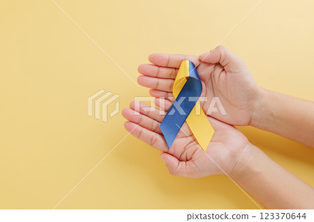 Down Syndrome and Autism Awareness globally. Yellow background with hands holding awareness ribbon 123370644