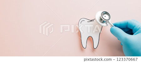 Dentist Day. Doctor hand in gloves checks a drawn paper tooth with a stethoscope on pink background 123370667