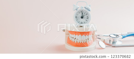 Dentist shows a teeth model with a white alarm clock and stethoscope Dentist shows a teeth model with a white alarm clock and stethoscope 123370682