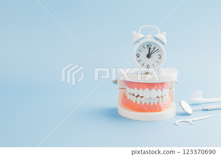 A Dentist presents a teeth model with a white alarm clock, emphasizing oral care, dentistry tools 123370690