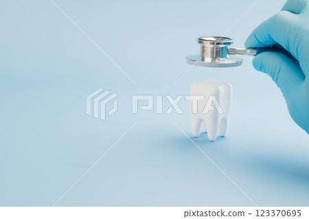 Dentist Day features a doctor using a stethoscope on a tooth model against blue Dentist Day features a doctor using a stethoscope on a tooth model against blue 123370695