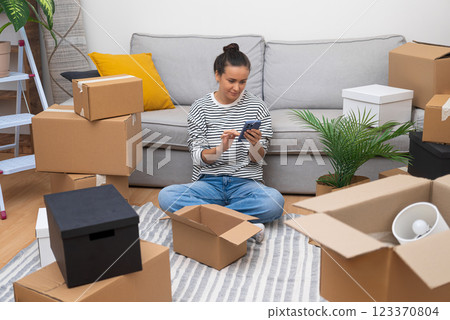 Young woman unpacks on moving day, stays connected with her phone in her new home, marking a new chapter 123370804
