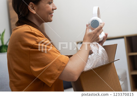 Seated comfortably, a lady explores her headphone delivery, expressing delight after a satisfying online shopping experience. Seated comfortably, a lady explores her headphone delivery, expressing delight after a satisfying online shopping experience. 123370815