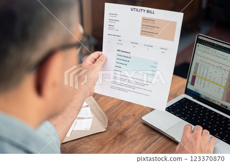 Man reviewing utility bill while working on laptop. Household finance and budget management concept.  123370870