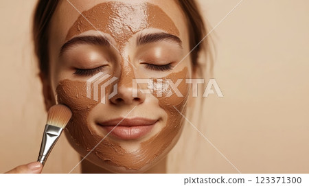Beautician applying a clay mask to a young woman's face with a brush. Her eyes are closed and she is enjoying the treatment 123371300