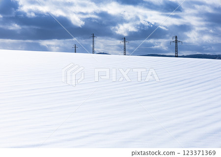 厚厚的雲層景觀、雪地上的風紋以及電力塔和輸電線的景觀 123371369
