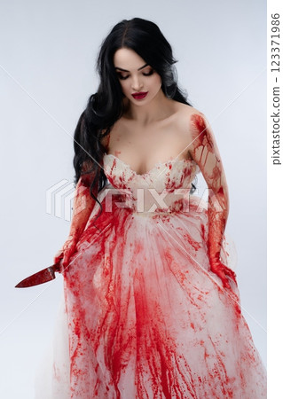 Bride in a blood-stained gown holds a knife, embodying beauty and terror 123371986