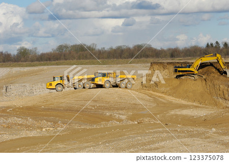 Yellow dump trucks and excavator are working in gravel pit 123375078
