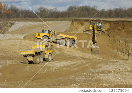 Yellow dump trucks and excavator are working in gravel pit 123375094