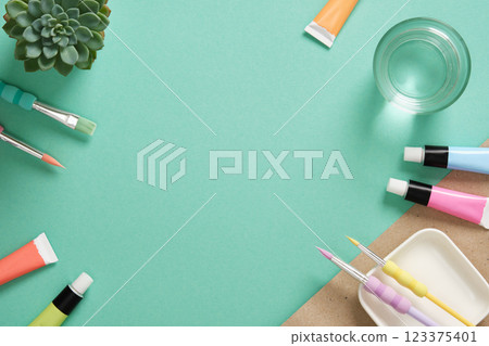 Preparing to painting. Tubes of acrylic paint, brushes, a glass of water on mint green background. Place for your text. 123375401